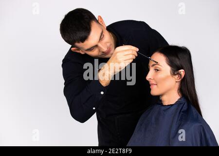 L'artista maschile del trucco fa il trucco per una donna di affari. Stereotipi di bellezza, moda e genere isolati su bianco. Foto Stock