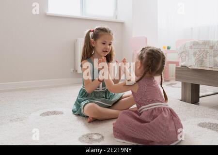 Carine piccole sorelle che giocano insieme seduta sul tappeto in abiti identici colori diversi in una stanza con molta luce Foto Stock