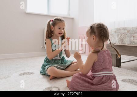 Carine piccole sorelle che giocano insieme seduta sul tappeto in abiti identici colori diversi in una stanza con molta luce Foto Stock