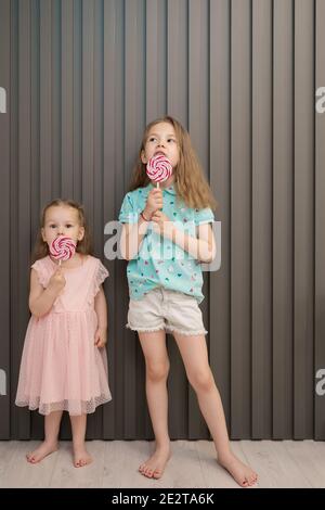 Felice giovane caucasica bambine bambini lick mangiare felice caramella dolce lollypop grande su sfondo grigio a strisce Foto Stock