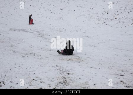 Adulto e bambino su una slitta che scivola giù la neve verso un altro bambino in fondo ad una collina in inverno Nello Yorkshire Foto Stock