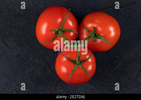 Tre pomodori rossi su un ramoscello verde su fondo di pietra nera. Vista dall'alto. Spazio di copia Foto Stock