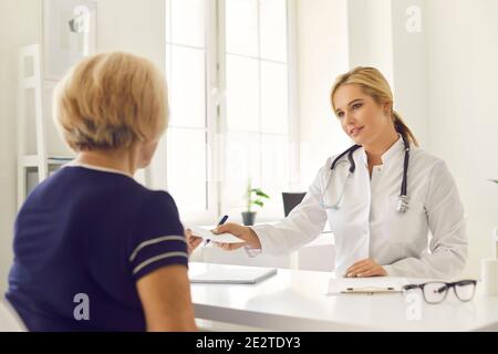 Un medico amichevole dà una prescrizione ad un paziente mentre si siede ad un tavolo nell'ufficio della clinica. Foto Stock