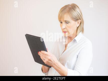 Ritratto di una donna anziana che usa un tablet digitale su sfondo bianco. Foto Stock