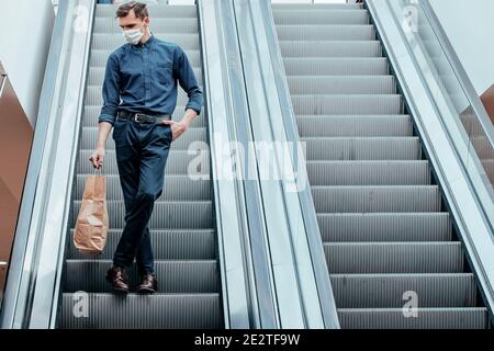 uomo in una maschera protettiva che si trova sulle scale mobili Foto Stock