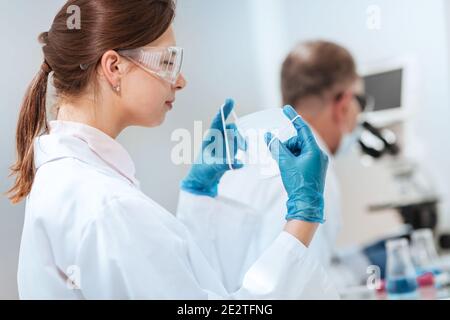 donna scienziata che mette su una maschera protettiva in laboratorio. Foto Stock