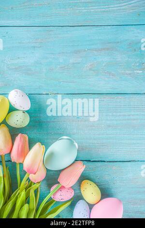 Primavera e Pasqua sfondo vacanze con fiori di tulipano, colorate uova pastello su tavolo blu vista dall'alto. Buon biglietto d'auguri pasquale. Foto Stock