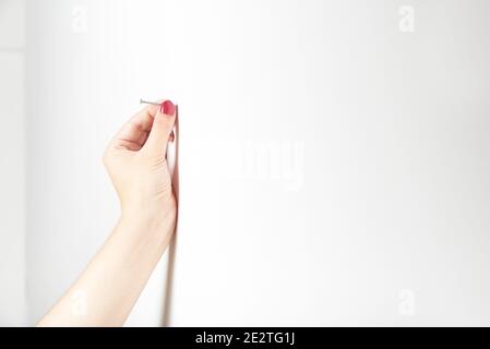 Mano curata di una giovane donna che tiene un chiodo nel muro, per martellarlo. Immagine luminosa con spazio per la copia. Foto Stock