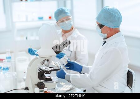 scienziati con campioni di nuovi farmaci seduti a un tavolo di laboratorio. Foto Stock