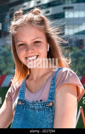 ragazza allegra e dai capelli rossi che ascolta la musica con le cuffie una giornata estiva di sole Foto Stock