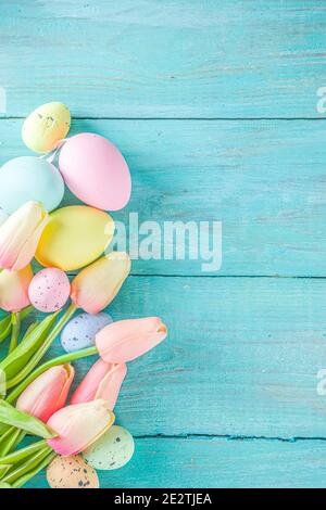 Primavera e Pasqua sfondo vacanze con fiori di tulipano, colorate uova pastello su tavolo blu vista dall'alto. Buon biglietto d'auguri pasquale. Foto Stock