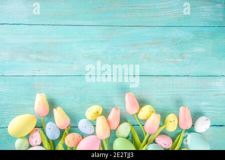 Primavera e Pasqua sfondo vacanze con fiori di tulipano, colorate uova pastello su tavolo blu vista dall'alto. Buon biglietto d'auguri pasquale. Foto Stock