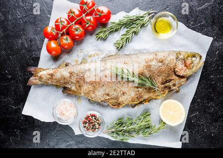 Trota al forno pesce con sale e limone e rosmarino su carta su sfondo nero Foto Stock