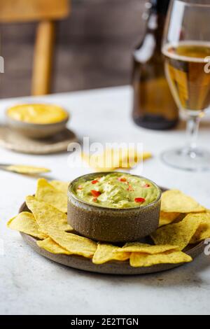 Patatine nachos in una ciotola con salse guacamole e birra su sfondo di pietra bianca. Foto Stock