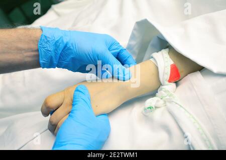 Il medico maschio palpate una vena del paziente prima di iniettare. Foto Stock