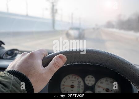 la mano di un uomo sul volante di un'auto che sta guidando su una neve coperta scivolosa strada invernale ghiacciata Foto Stock