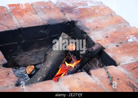 Fuoco brucia in vecchio camino tradizionale di pietra di mattoni. Legna e fiamme in fiamme. Camino esterno in inverno.