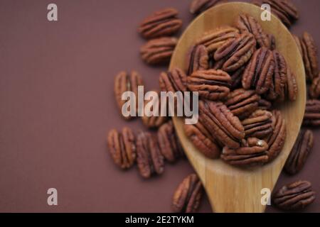 Noce di pecan in cucchiaio su sfondo bruno brillante.healthy grasses.Heap guscio di noce di pecan sgusciato. Ingrediente del keto diet.Tasty cibo organico crudo e. Foto Stock