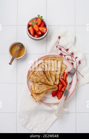 Crepes pancake con formaggio spalmabile, fragola fresca e miele per colazione in un bel piatto di ceramica bianca. Spazio per testo o ricetta. Vista dall'alto. Foto Stock