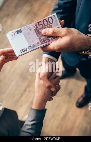 Visione tagliata dell'investitore che dà le banconote in euro e handshaking con donna d'affari su sfondo sfocato Foto Stock