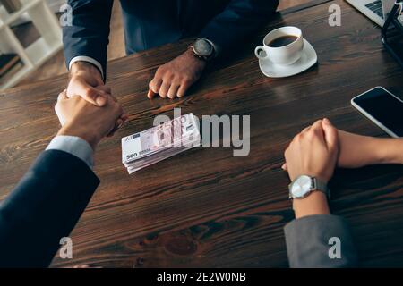 Vista tagliata di investitori e imprenditori handshaking vicino alle banconote in euro e la donna d'affari in primo piano offuscato Foto Stock