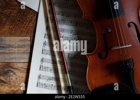 Violino, note musicali e piatto di prua su sfondo ligneo. Ombre forti. Foto Stock