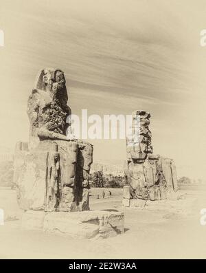 Luxor. Questo è il sito archeologico del 1350 a.C. presso i Colossi di Memnone dell'Antico Egitto, non lontano dal fiume Nilo e dalla città di Luxor precedentemente conosciuta come Tebe. Le statue sono del faraone Amenhotep III, ci sono due statue più piccole ai suoi piedi, una è sua madre, l'altra sua moglie. Inizialmente costruiti per proteggere l'ingresso al tempio di Amenotep contro il male, sono stati anche visti per proteggere la riva occidentale del Nilo. I Colossi hanno sofferto di gravi danni sismici, ma dopo 3500 anni rimangono in piedi. Foto Stock