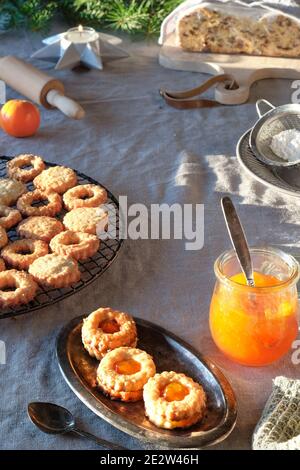 Yummy Linzer biscotti riempiti con marmellata d'arancia su griglia di raffreddamento e piatto di metallo vintage. Xmas stollen su tavolo con tovaglia di lino naturale. Natale Foto Stock