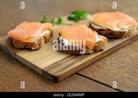 Panini aperti con pane di fichi e salmone affumicato sulla panna su un tagliere di legno, primo piano fuoco selettivo Foto Stock