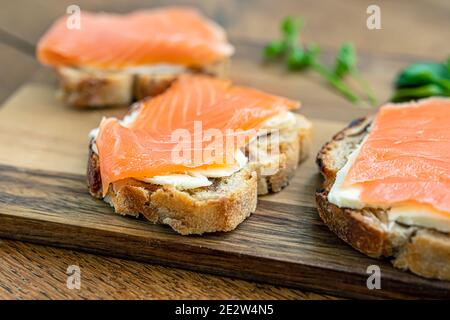 Cibo sano, toast di pane di fichi con formaggio cremoso e salmone affumicato su tavola da taglio in legno primo piano fuoco selettivo Foto Stock