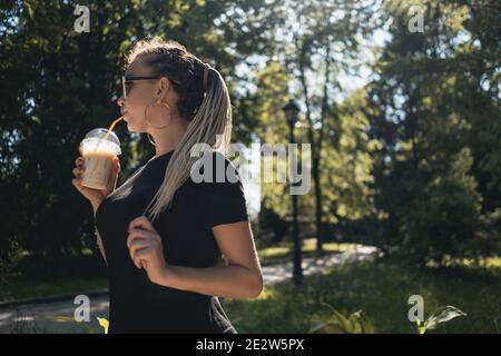 giovane bella femmina intrecciata bere milkshake con caramello in parco soleggiato Foto Stock