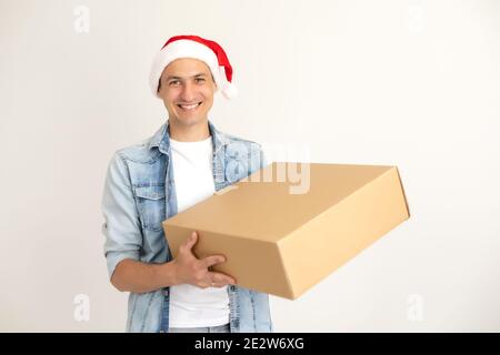 Ridendo uomo di consegna in cappello di babbo natale sul telefono, in piedi e tenendo scatola di cartone su una mano. Isolato su bianco. Foto Stock