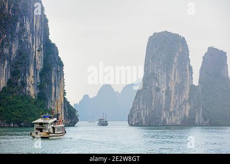 Barche turistiche e isole monolitiche di pietra calcarea a ha Long Bay / Baia di ha Long / Vinh ha Long nella nebbia, provincia di Quang Ninh, Vietnam Foto Stock