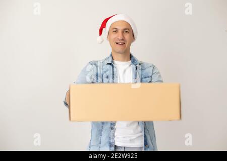 Ridendo uomo di consegna in cappello di babbo natale sul telefono, in piedi e tenendo scatola di cartone su una mano. Isolato su bianco. Foto Stock