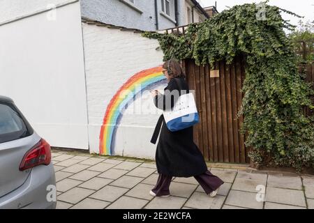 Una donna passa accanto a un colorato arcobaleno dipinto su un muro bianco a West Norwood, nel sud di Londra, Inghilterra. Foto di Sam Mellish Foto Stock