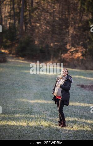 Felice giovane donna incinta in piedi fuori in natura tenendo la sua pancia grande in tarda gravidanza. Foto Stock