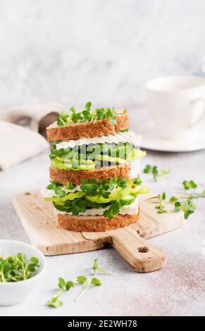 Sandwich di avocado, cetriolo e formaggio feta decorato con micro-verdi e pane a grani multipli su un semplice piedistallo in legno per una sana colazione. Selez Foto Stock