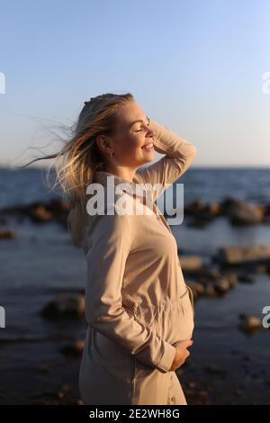 Felice donna incinta vicino al mare in estate. Foto Stock