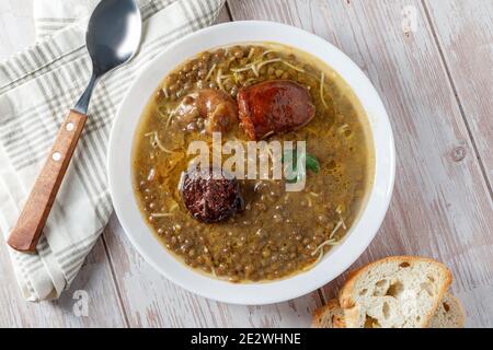 Lenticchie con chorizo, salsiccia di sangue e verdure, in piatto caldo su tavola di legno Foto Stock