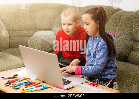 Due bei bambini felici sorridenti carini, un ragazzo e una ragazza, usano il laptop per imparare a distanza o per l'intrattenimento. Foto Stock