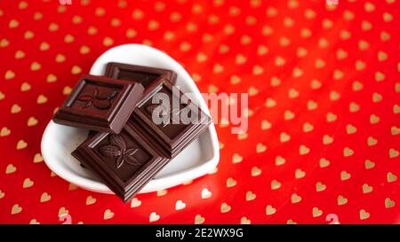 Cioccolato nero in una piastra a forma di cuore su sfondo rosso Foto Stock