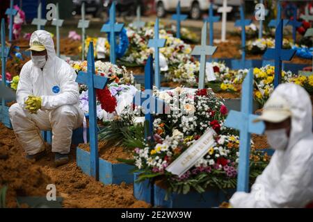 Manaus, Brasile. 15 gennaio 2021. I lavoratori del cimitero in tute protettive si siedono su tombe decorate con fiori durante un funerale al cimitero di Nossa Senhora Aparecida. Solo nello stato di Amazonas sono stati confermati 223,360 casi di Covid 19. Manaus, la capitale dello stato, ha registrato l'ultima volta il maggior numero di ricoveri legati a Covid-19 dall'aprile 2020, e il sistema sanitario locale era crollato. L'aeronautica brasiliana ha dovuto fornire ossigeno nella regione. Credit: Lucas Silva/dpa/Alamy Live News Foto Stock