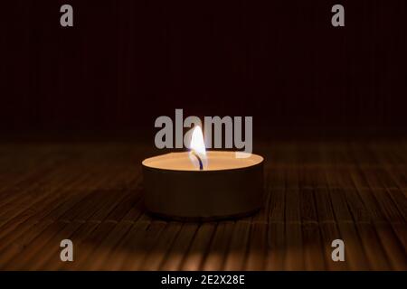 candela che brucia su uno sfondo di legno. Primo piano di una sola luce del tè al buio Foto Stock