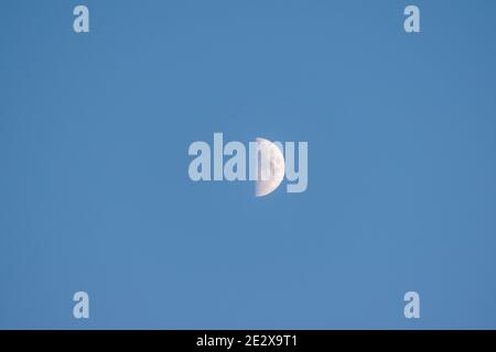 Primo piano di un quarto di luna in un cielo azzurro limpido e senza nuvole al tramonto, Ericeira, Portogallo. Foto Stock