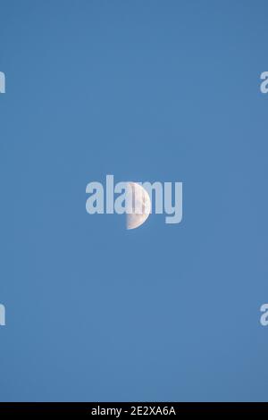 Primo piano di un quarto di luna in un cielo azzurro limpido e senza nuvole al tramonto, Ericeira, Portogallo. Foto Stock