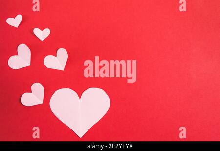 Cuori di carta di diverse dimensioni su sfondo rosso. Sfondo astratto con forme tagliate in carta. San Valentino, giorno della madre. Compleanno saluto Foto Stock