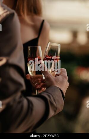 Coppia d'amore che si tiene insieme e porta bicchieri con champagne frizzante e confetti a forma di cuore rosso. Il concetto di matrimonio, giorno degli amanti. Felice Foto Stock