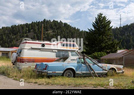 Un vecchio RV e Lincoln Continental parcheggiati in un lotto sopravcresciuto nella piccola città di Basin, Montana. Foto Stock