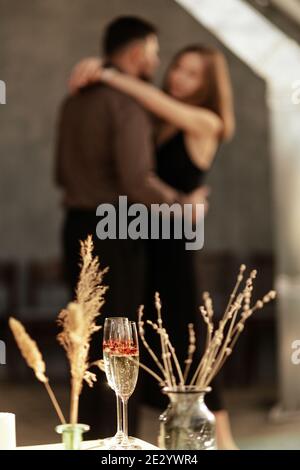 Una coppia ben vestita che danzano a casa. Il concetto di matrimonio, giorno degli amanti. Primo piano su bicchieri con champagne frizzante e a forma di cuore rosso Foto Stock