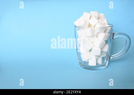 Tazza trasparente piena di raffinati cubetti di zucchero bianco su sfondo blu. Spazio di copia Foto Stock